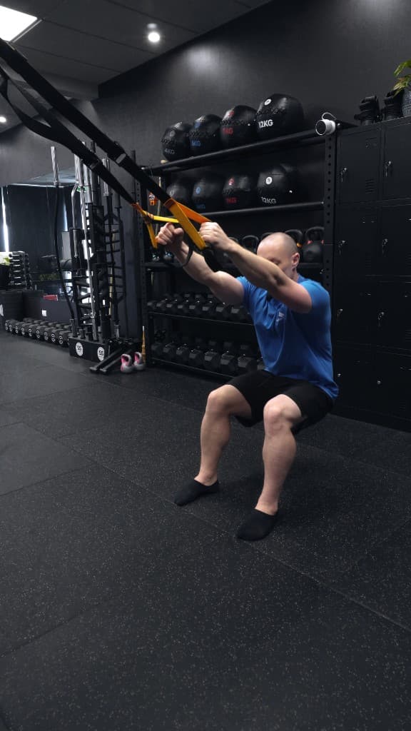 Deep squat using suspension trainer straps at Iron Focus Gym